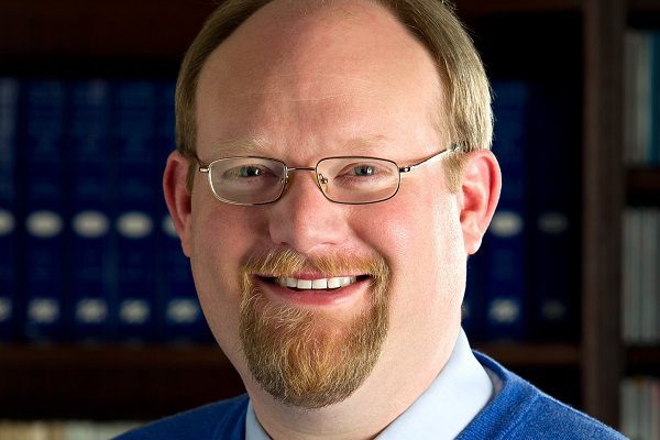 Headshot of James Grymes against a blue background